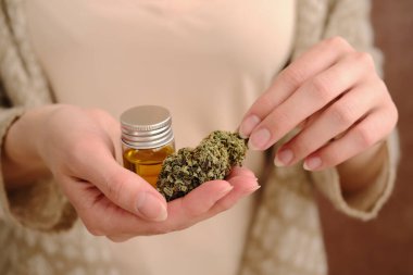 Esrar tomurcuğu ve cbd yağını genç bir kadının kahverengi arka planına yakın tut. Tıbbi marijuana kullanımı kavramı.