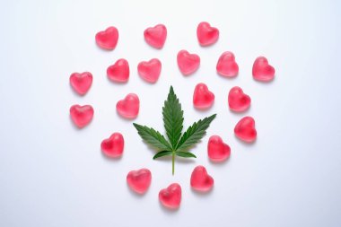 Marihuana ve seks konsepti. Gri izole bir zemin üzerinde kalp şeklinde şekerler bulunan kenevir yaprağı. CBD lolipopları. Sevgililer Günü konsepti
