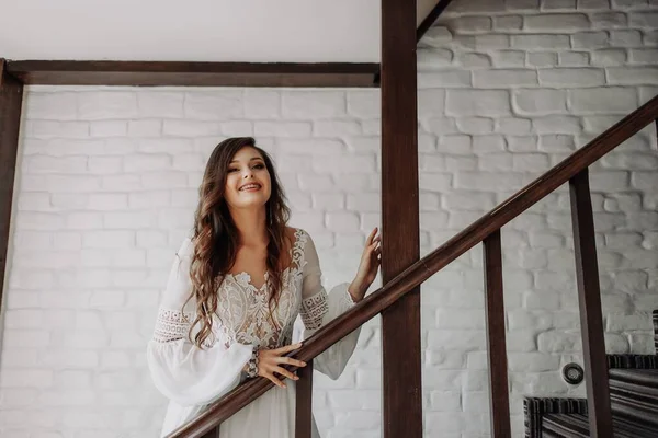 戴牙套的女孩在笑 一位身穿长发的白色婚纱的新娘站在木制楼梯上微笑着 等待着她的丈夫 — 图库照片