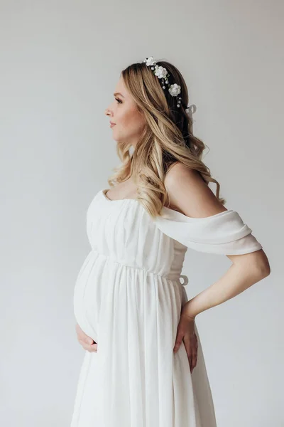 Blondynka Ciąży Białej Sukience Wieńcem Głowie Studio Białym Tle Trzyma — Zdjęcie stockowe