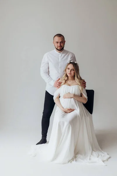 Manžel Těhotná Blondýna Manželka Bílých Šatech Ateliéru Bílém Pozadí Věncem — Stock fotografie
