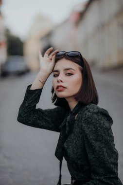 Siyah gözlüklü, kısa siyah elbiseli esmer bir kız şehirde yürüyor.