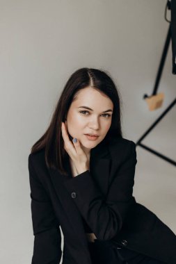Girl in a black suit on a white background sits on the floor