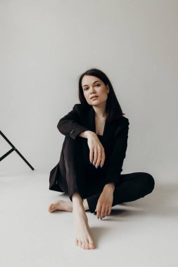 Girl in a black suit on a white background sits on the floor
