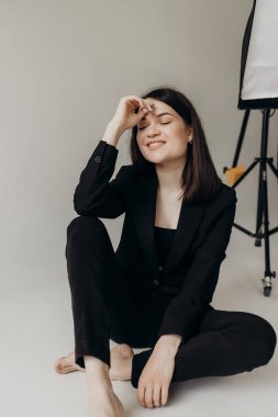 Girl in a black suit on a white background sits on the floor