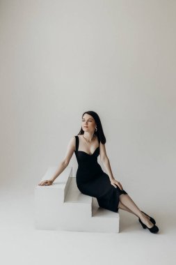 A girl in a black dress on a white background sits on the steps
