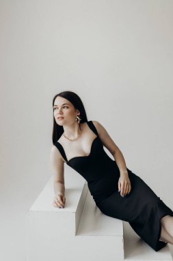 A girl in a black dress on a white background sits on the steps