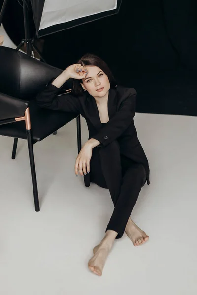 Girl Black Suit White Background Sits Floor Chair — Zdjęcie stockowe
