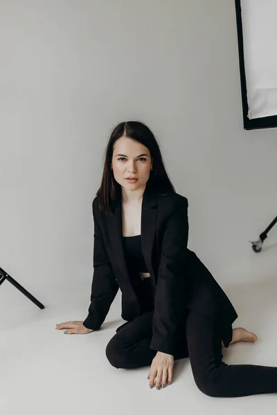 Girl Black Suit White Background Sits Floor — Zdjęcie stockowe