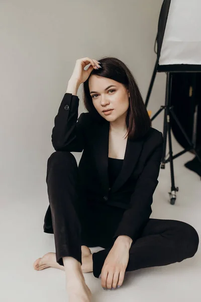 Girl Black Suit White Background Sits Floor — Zdjęcie stockowe