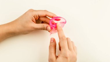 Kadın elleri bej arka planda Silikon Regl Kupasını katlıyor. Konforlu ve Sıfır Atık Kadın Döngüsü Dönemi İçin Hijyenik Araç