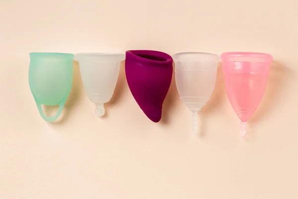 Five Menstrual Cups Different Size Shapes Colors Row Beige Background — стоковое фото