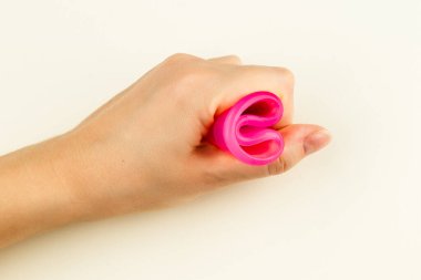 Female hand holding a pink Menstrual Cup folded with a C-Fold Method. Folding Menstrual Cup is for comfortable inserting it into vagina to collect blood during woman periods