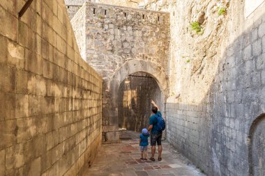 Baba ve oğul Karadağ 'ın Kotor kentindeki ortaçağ kale duvarları arasında yürüyorlar. Turistler, güneşli bir yaz gününde eski kentte dar kaldırımlı taş caddeleri keşfediyorlar..