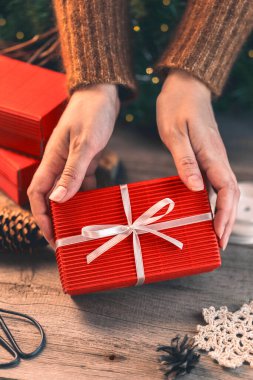 Kırmızı Noel hediye kutusunu beyaz kurdeleyle süsleyen kadın elleri.