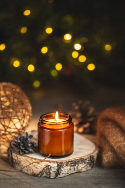 Arkaplanda koyu cam bir kavanozda yanan aroma mumu ve bulanık bokeh ışıkları olan rahat bir kış akşamı kartı. Yumuşak odak, metin için alanı kopyala. Evde Noel tatili.