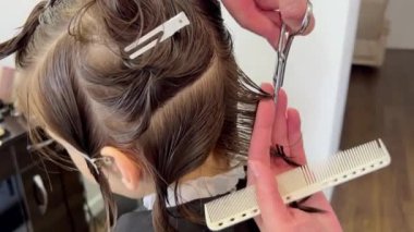 Professional Hairdresser doing haircut for kid in the barbershop. Close up video of white boy having hairstyle at the hair salon