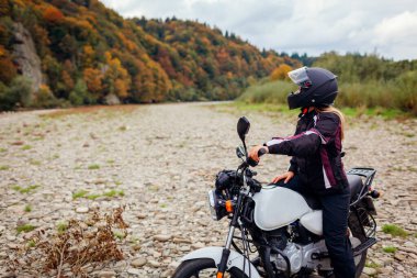 Kadın motorcu sonbaharda motosikletle seyahat eder. Motosikletçiler ormanda dinlenerek sonbahar manzarasının tadını çıkarırlar. Motosiklette oturan gezgin, kask ve ceket giyiyor.