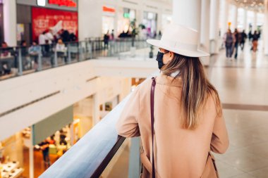 Alışveriş merkezinde çanta taşıyan Coronavirus Covid yüzünden maske takan şık bir kadının portresi. Sonbahar salgını modası