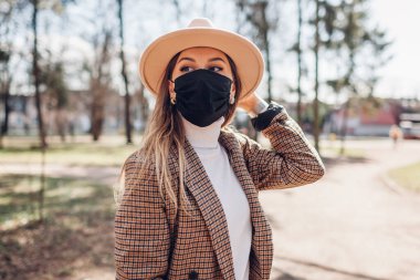 Boş parkta Coronavirus covid-19 salgını sırasında açık havada yeniden kullanılabilir maske takan şık bir kadının portresi. Bahar modası