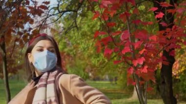 Sonbahar parkında yürüyen ve dans eden koruyucu maskeli mutlu bir kadın. Covid-19 salgını
