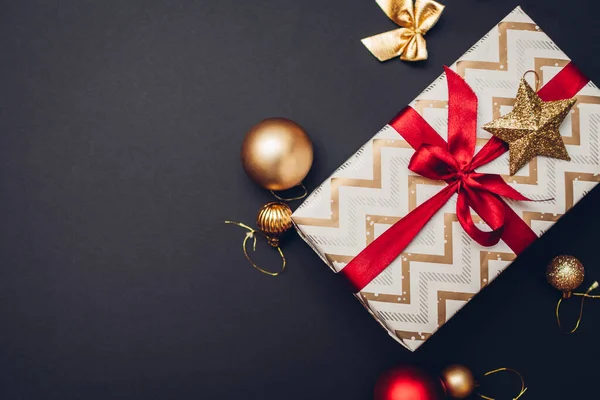 クリスマスと新年のプレゼントは 休日の紙に包まれ 黒を背景に赤いリボンと黄金の装飾品 おもちゃ ボールで飾られています スペース — ストック写真