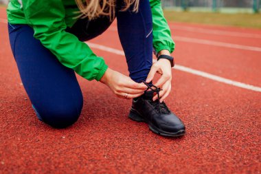 Koşu pistinde ayakkabı bağcıkları bağlayan bir koşucu. Sonbahar spor sahasında kadın antrenmanı. Aktif, sağlıklı, sportif yaşam tarzı. Sonbahar aktiviteleri.