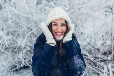 Kış aktiviteleri. Kış parkında yürüyen genç bir kadın kalın giysiler giymiş kar ve soğuğa hayranlık duyuyor. Mutlu kız dışarıda eğleniyor..