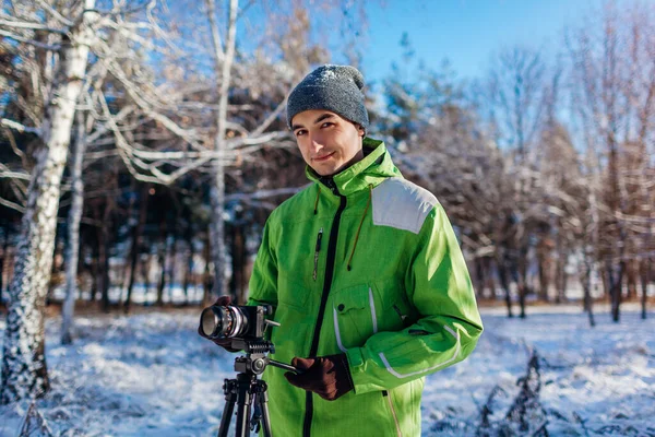 年轻的摄影师用相机和三脚架拍摄雪地冬季森林景观的照片和录像 户外季节性业余活动 — 图库照片