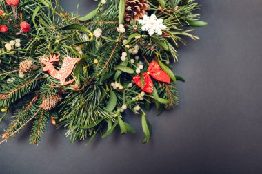 Noel ve Yeni Yıl çelenkleri köknar, çam, ökseotu dalları, kırmızı süslemelerle süslenmiş koniler, gri arka planda oyuncaklar, fiyonklar.