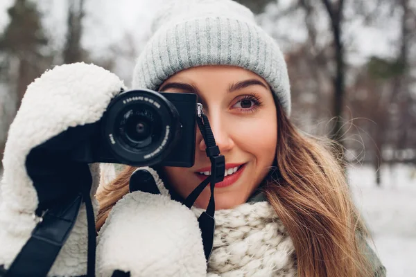 Молода жінка-фотограф фотографує засніжений зимовий парк, використовуючи камеру в теплому одязі. Зовнішня діяльність — стокове фото