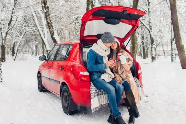 Sevgili çift arabanın bagajında oturmuş, karlı kış ormanlarında sıcak çay içiyorlar. Tatillerde insanlar dışarıda dinleniyor.
