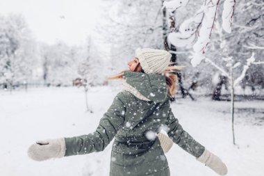 Karlı kış parkında karla oynayan, kalın örgülü kıyafetler giyen ve dışarıda eğlenen mutlu genç bir kadın. Mevsimlik faaliyetler