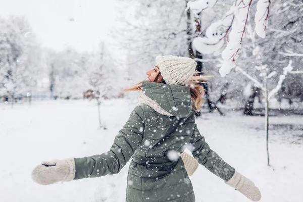 Karlı kış parkında karla oynayan, kalın örgülü kıyafetler giyen ve dışarıda eğlenen mutlu genç bir kadın. Mevsimlik faaliyetler