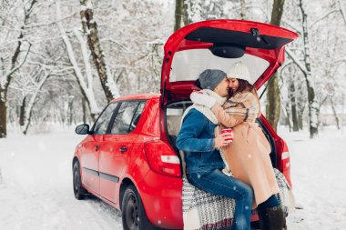 Sevgili çift arabanın bagajında dinleniyor. Karlı kış ormanlarında sıcak çay içiyorlar. Tatillerde insanlar dışarıda dinleniyor.
