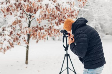 Fotoğrafçı, karlı kış parkında tripodun üzerinde profesyonel dijital kamera kullanarak fotoğraf çekiyor. Manzara resimleri. Açık hava fotoğrafçılığı