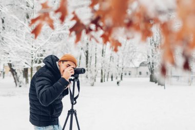 Fotoğrafçı, karlı kış parkında tripodun üzerinde profesyonel dijital kamera kullanarak fotoğraf çekiyor. Manzara resimleri. Açık hava fotoğrafçılığı. Hobi