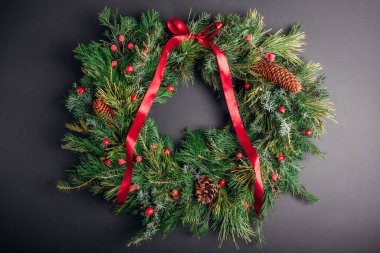 Noel ve Yeni Yıl çelengi köknar, çam ladini her zaman yeşil dallar, gül kalçalar, gri arka planda kırmızı kurdele ile süslenmiş koniler..
