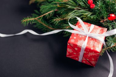 Noel ve Yeni Yıl hediye paketi, Noel kağıdı ve kurdeleye sarılmış, köknar çelengi. Siyah arka planda kış tatili için mevcut