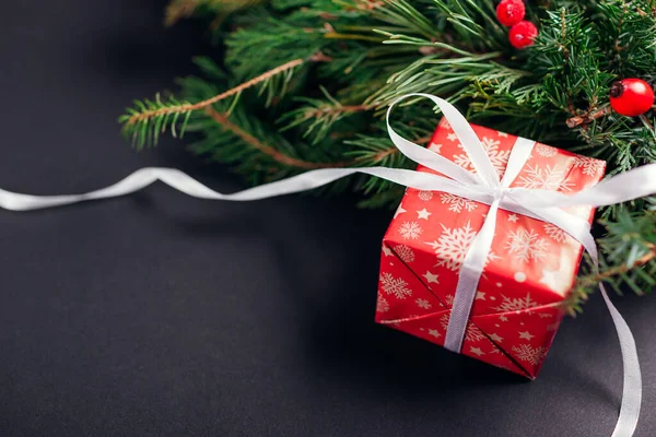 Noel ve Yeni Yıl hediye paketi, Noel kağıdı ve kurdeleye sarılmış, köknar çelengi. Siyah arka planda kış tatili için mevcut