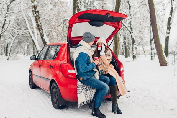 可爱的夫妻坐在汽车行李箱里 在雪地的冬季森林里喝着热茶 外出度假期间外出度假的人 — 图库照片