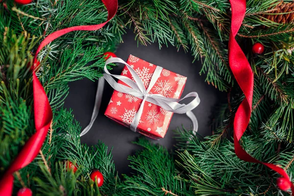 クリスマスと新年の赤いギフトボックスは リボンとモミの花輪の内側にお祝いの紙とリボンで包まれています 黒を背景に冬の休日のために存在します トップ表示 — ストック写真