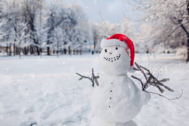 Karlı kış parkında Noel Baba şapkası takan mutlu bir kardan adam. Kış aktiviteleri. Boşluk