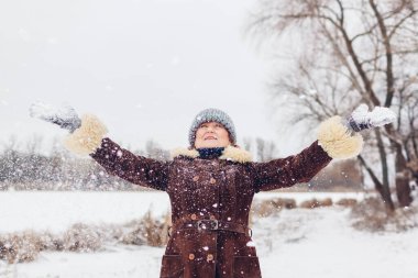 Portrait of happy senior woman throwing snow in snowy winter park. Having fun outdoors playing in park during walk. Seasonal activities