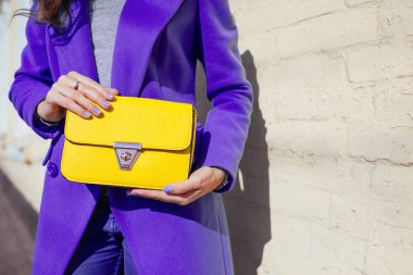Close up of stylish yellow handbag. Young woman wearing trendy purple coat. Spring female clothes and accessories. Fashion