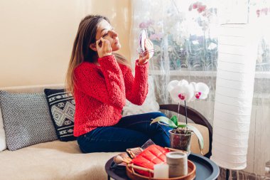 Evde aynaya bakarak makyaj yapan genç bir kadının portresi. Yanakları allık içinde fırça kullanan kız