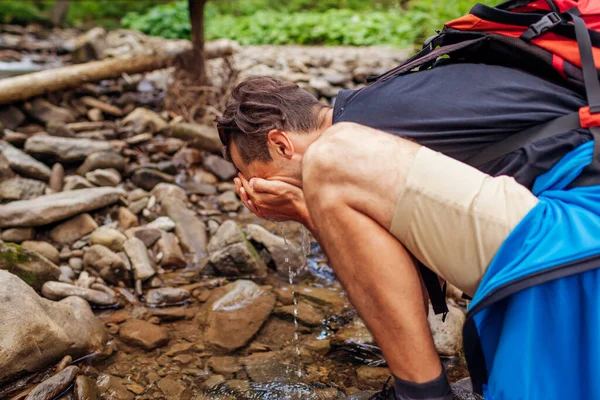 旅行者背着背包在喀尔巴阡山脉森林的山川桥面上洗脸 游客在被夏日自然包围的溪流中休息 — 图库照片