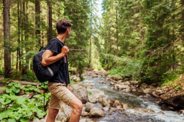 Sırt çantalı gezgin, Karpat ormanlarındaki dağ nehri kıyısında manzaranın tadını çıkarıyor. Ukrayna 'ya yaz gezisi. Sportif aktif yaşam tarzı
