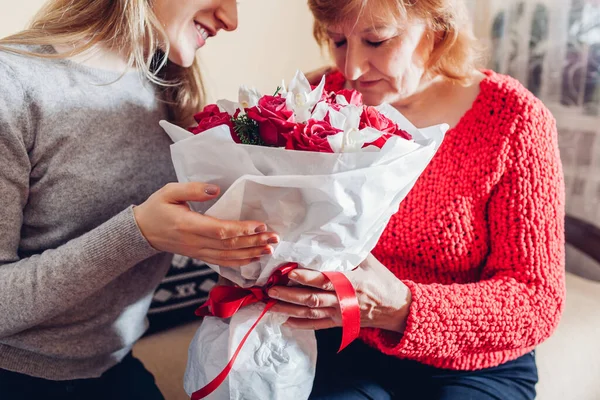 Filha dando sua mãe buquê de flores em casa como Mães presente do dia. Sênior mulher cheirando rosas — Fotografia de Stock