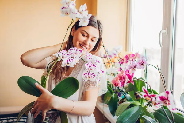 Улыбающаяся женщина наслаждается цветущей белой орхидеей с фиолетовыми точками, держащими горшок. Садовник заботится о домашних растениях и цветах. — стоковое фото